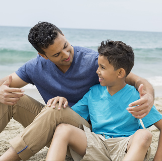 Father sitting with his arm around his early teenage son having a conversation.